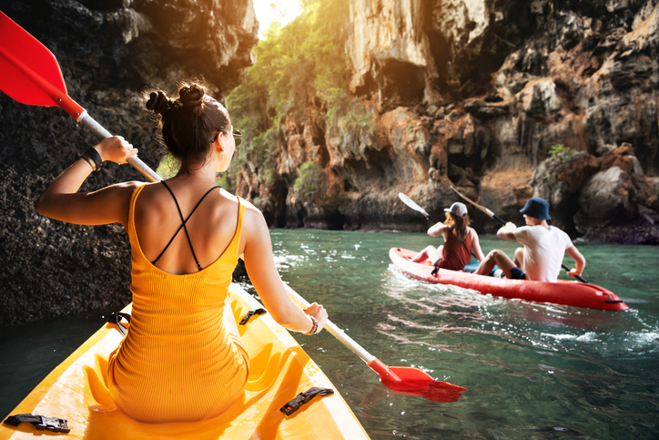 Woman and friends walks by kayaks at sea bay between big rocks