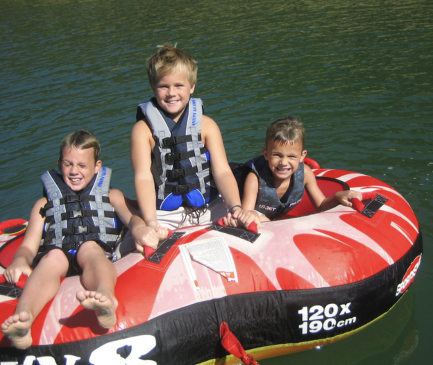 A group of children all riding a tube in the water at the lake